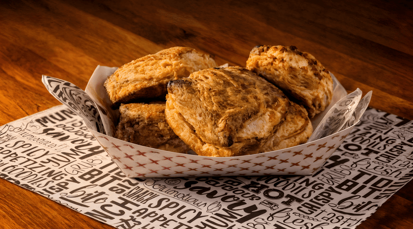 Golden brown biscuits in a paper tray, resting on a black and white patterned paper on a wooden table.