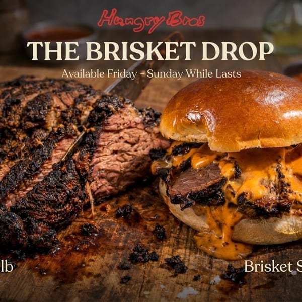 A large, smoked brisket is sliced on a wooden board next to a brisket sandwich with melted cheese.