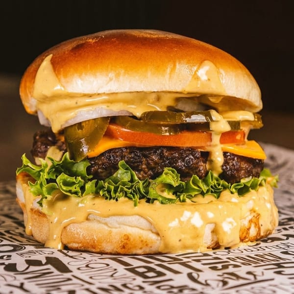 A juicy burger with melted cheese, lettuce, tomato, onions, and jalapeños, drizzled with sauce.