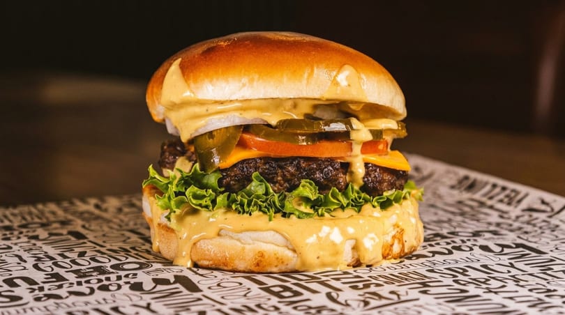 A juicy burger with melted cheese, lettuce, tomato, onions, and jalapeños, drizzled with sauce.