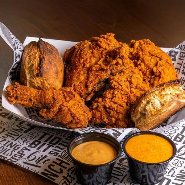Crispy fried chicken pieces and two baked potatoes in a paper-lined basket with two dipping sauces.