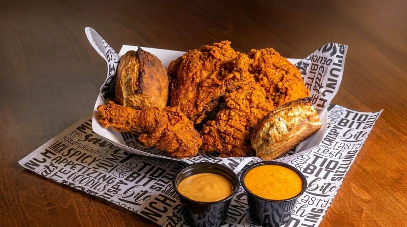 Crispy fried chicken pieces and two baked potatoes in a paper-lined basket with two dipping sauces.